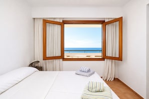 A hotel room with a bed, a chair, a window with curtains, and a view of the sea. - Exclusive Seafront Villa with Pool & Panoramic Views (Santa Ponça)