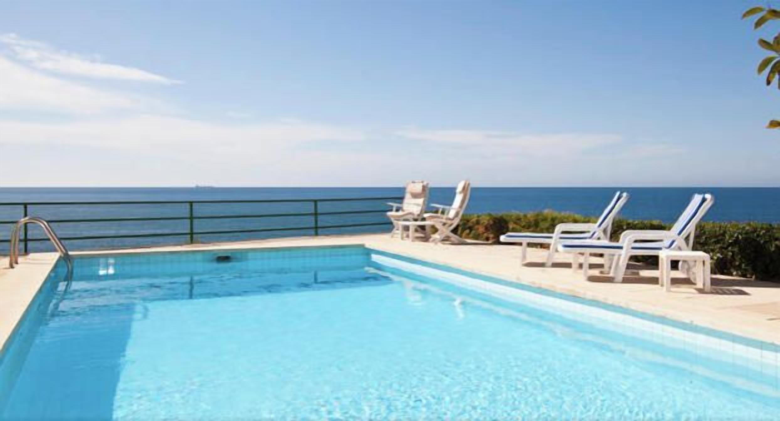 A swimming pool with a view of the sea, accompanied by lounge chairs.