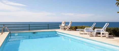 A swimming pool with a view of the sea, accompanied by lounge chairs.