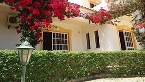 A building with a white facade, multiple windows, and a green hedge in the foreground. - 3 bed Villa with Private Pool and Gardens- sleeps 6/8. 5min stroll to village.  (Olhos'de agua)