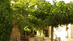 A courtyard with a stone wall, a wooden bench, a table, and chairs.