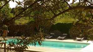 A swimming pool with lounge chairs and a stone wall in the background.