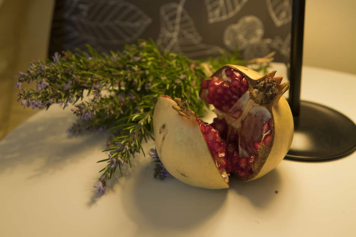 Una granada sobre una mesa con una lámpara y un papel tapiz estampado al fondo.