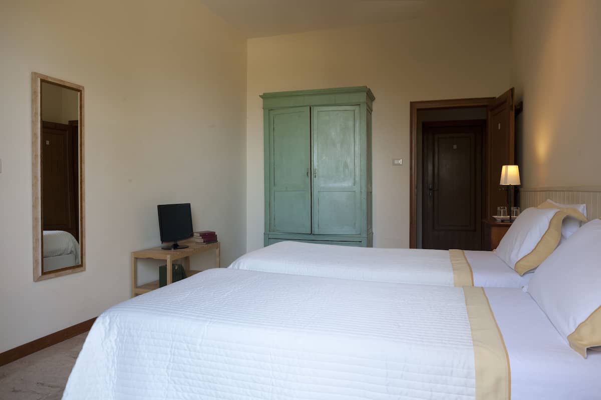 Habitación de hotel con dos camas, un televisor sobre una mesita, un armario verde y una puerta con una lámpara a su lado.