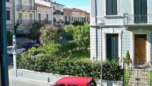 A residential street with a row of light-colored buildings, a red car parked on the side, and a clear blue sky. - Apartment near the sea with garage (Viareggio)