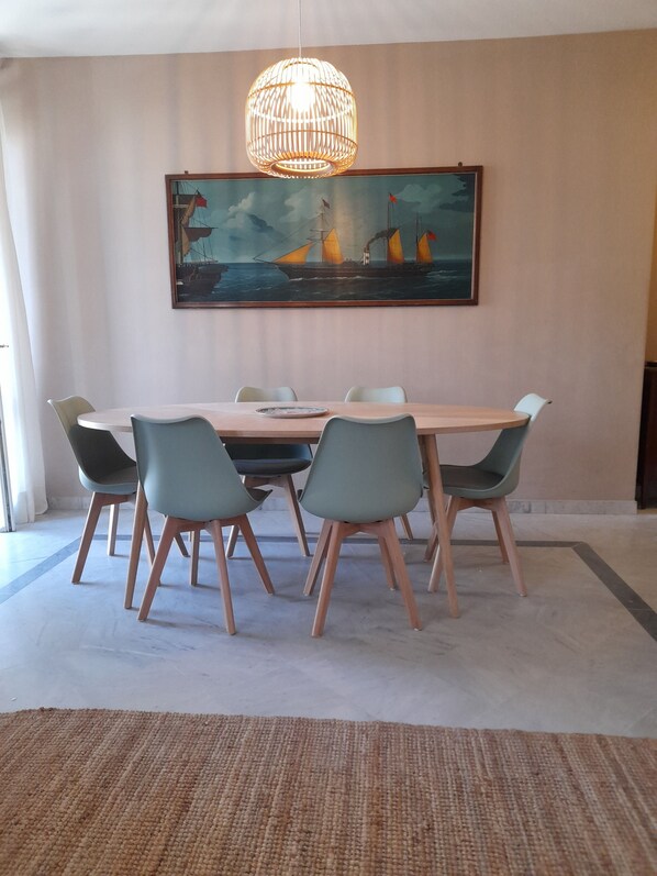 A dining area with a wooden table, six chairs, a woven rug, and a large painting of a ship on the wall. - Apartment near the sea with garage (Viareggio)