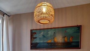 A dining area with a wooden table, four chairs, a hanging light fixture, and a maritime painting on the wall. - Apartment near the sea with garage (Viareggio)