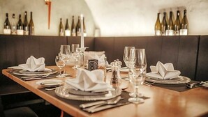 A restaurant setting with a long table set for dining, wine bottles on the wall, and a modern interior design. - Rodderhof (Bad Neuenahr-Ahrweiler)