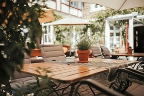 An outdoor patio with wooden tables and chairs, potted plants, and umbrellas. - Rodderhof (Bad Neuenahr-Ahrweiler)
