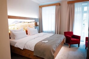A hotel room with a large bed, two red chairs, a wooden headboard, and a view of a field through the window. - Rodderhof (Bad Neuenahr-Ahrweiler)