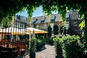 Un patio con edificios de piedra, mesas al aire libre y plantas en macetas.