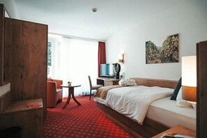 A hotel room with a bed, a TV, a desk, a chair, and a window with curtains.