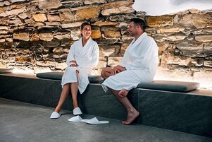 Dos personas vestidas de blanco sentadas en un muro de piedra.