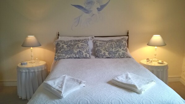A neatly made bed with two pillows, two bedside tables with lamps, and a wall with a painting.