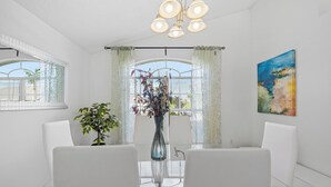 Ein Essbereich mit einem Glastisch, weißen Stühlen, einer Vase mit Blumen und einem Gemälde an der Wand.