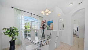 Ein Essbereich mit einem Glastisch, weißen Stühlen, einem Blumentopf und einem Bild an der Wand.