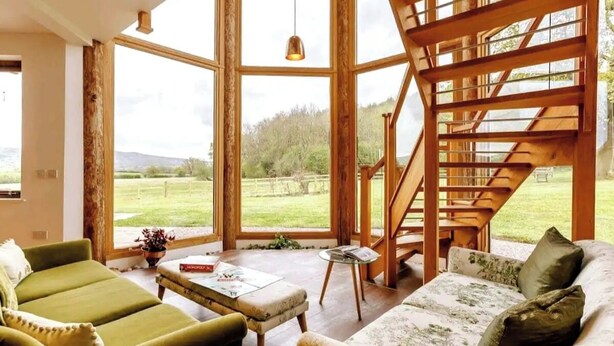 Ein geräumiges Zimmer mit großen Fenstern, einer Holztreppe und einem grünen Sofa.