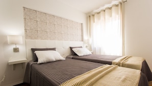Habitación de hotel con dos camas, cabecero con panel decorativo, lámparas de noche y una ventana con cortinas.