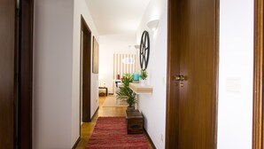 Un pasillo con piso de madera, un tapete rojo, una planta en maceta y una rueda decorativa colgada en la pared.