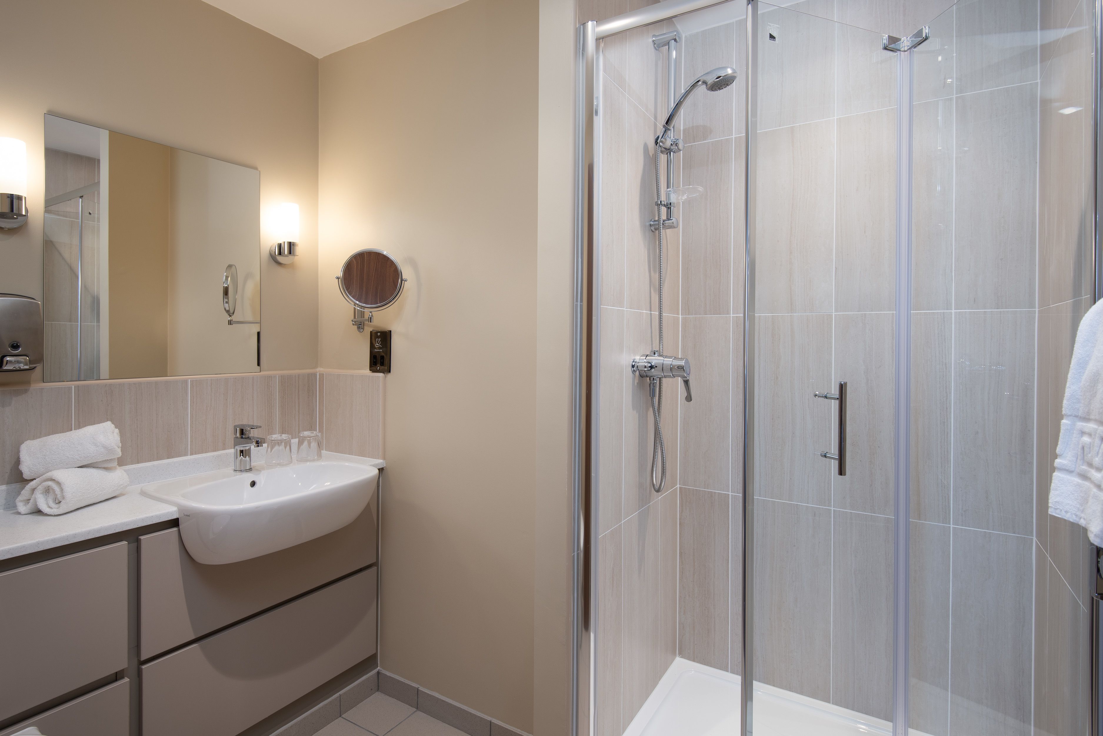 A modern bathroom with a large mirror, a sink, and a glass-enclosed shower area.