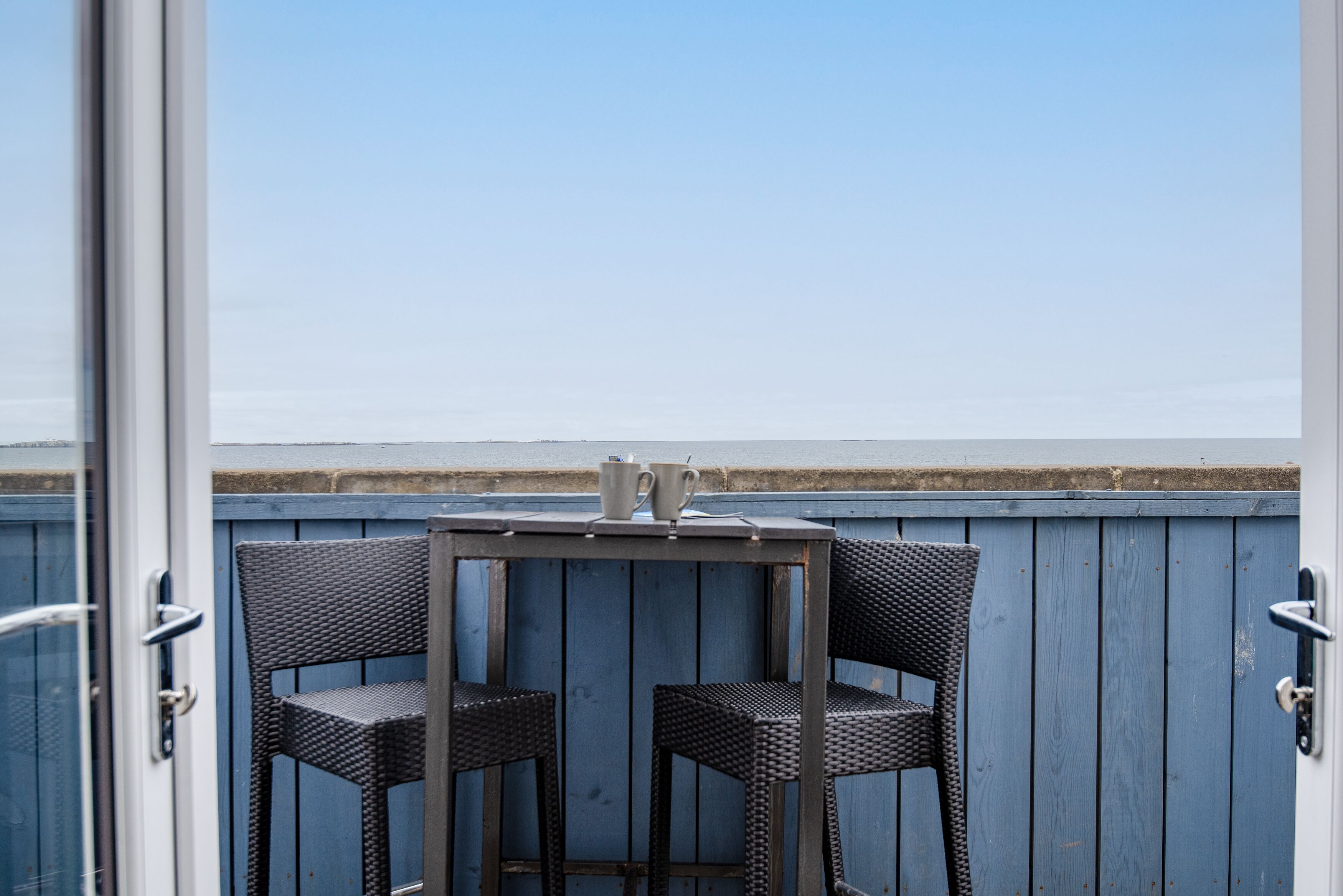 An outdoor seating area with two wicker chairs and a small table, overlooking a coastal landscape.