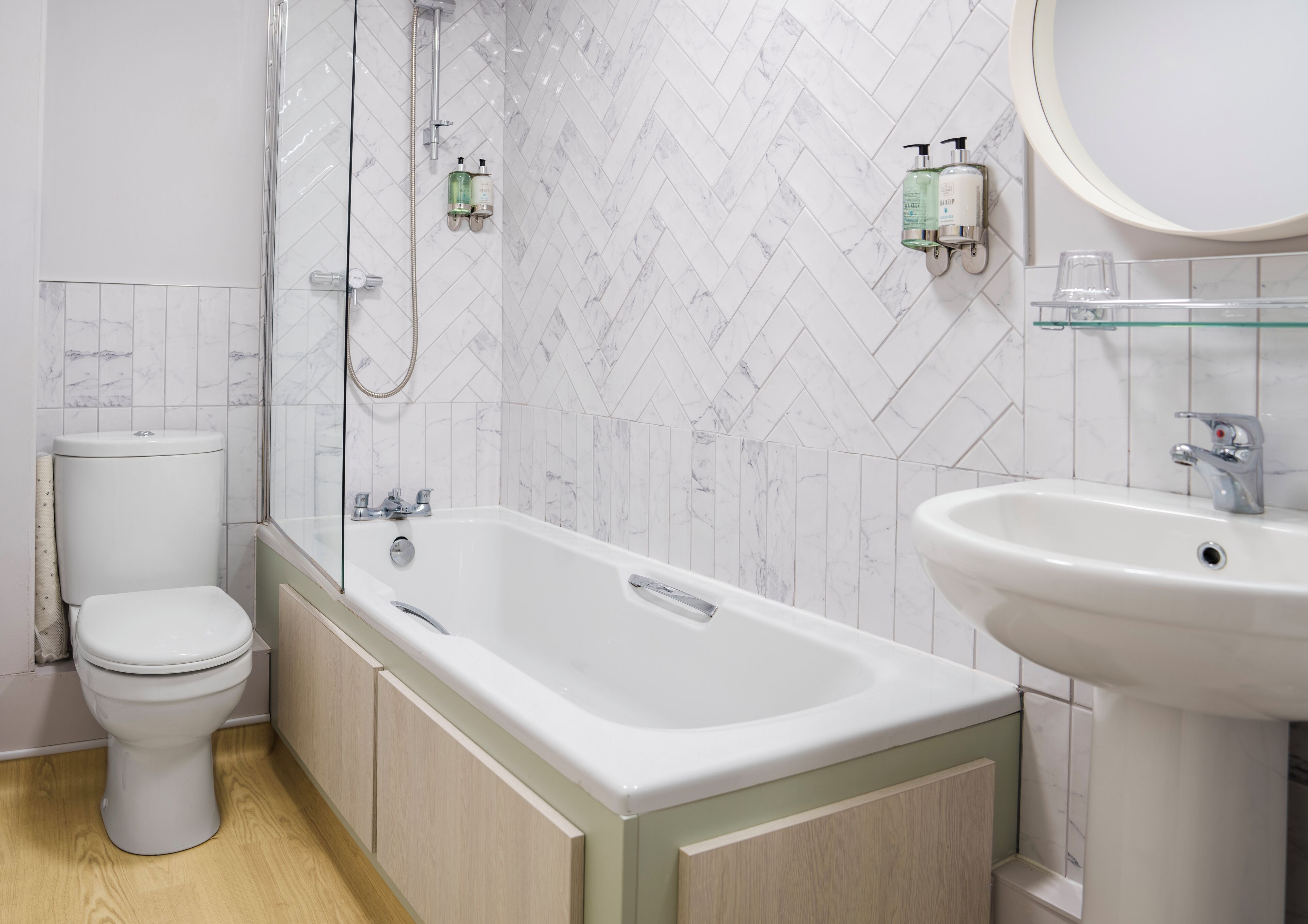 A modern bathroom with a white toilet, a freestanding bathtub, and a sink with a glass shelf.