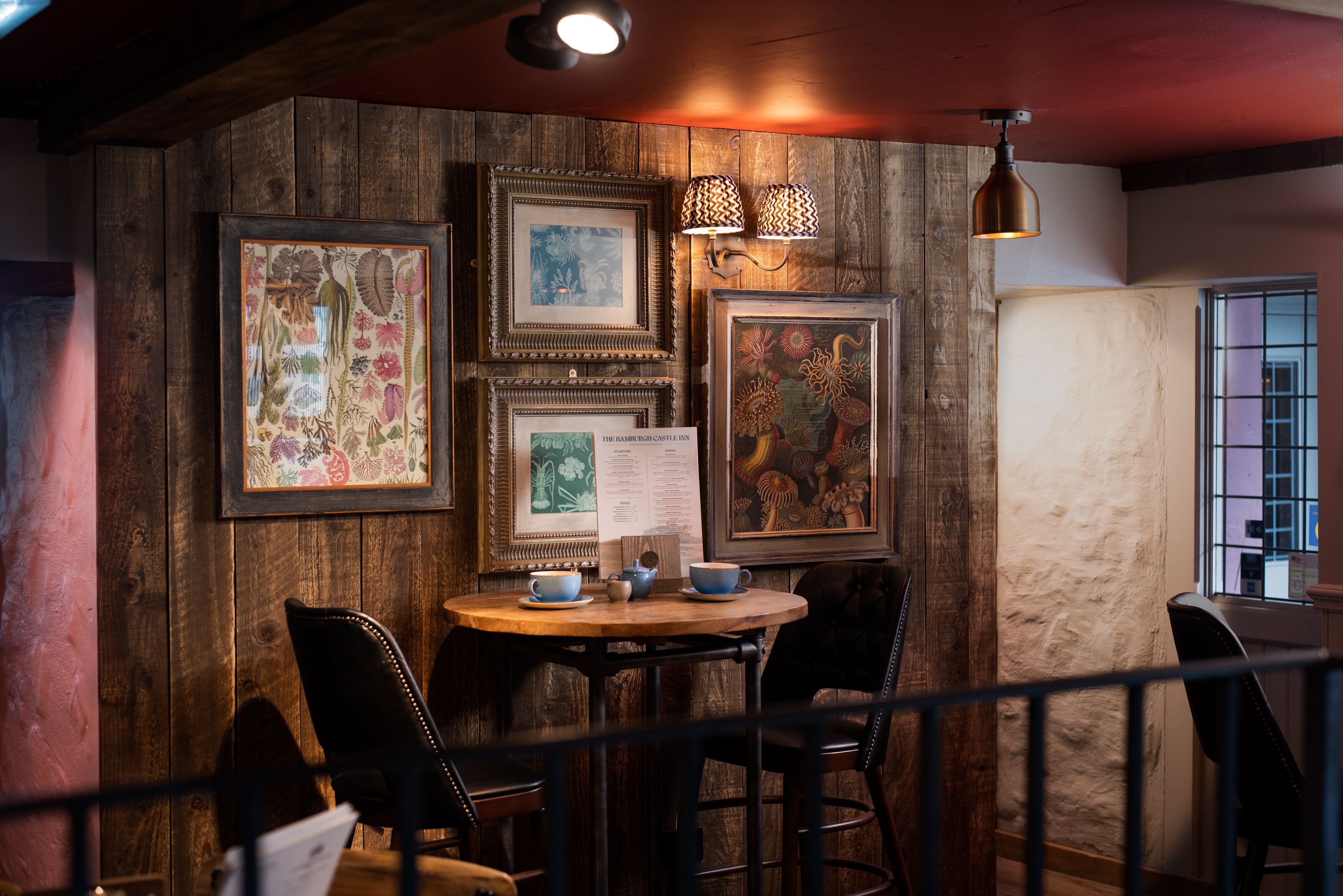 Ein Holzinterieur mit einem runden Tisch, Stühlen und gerahmten Pflanzenbildern an der Wand.