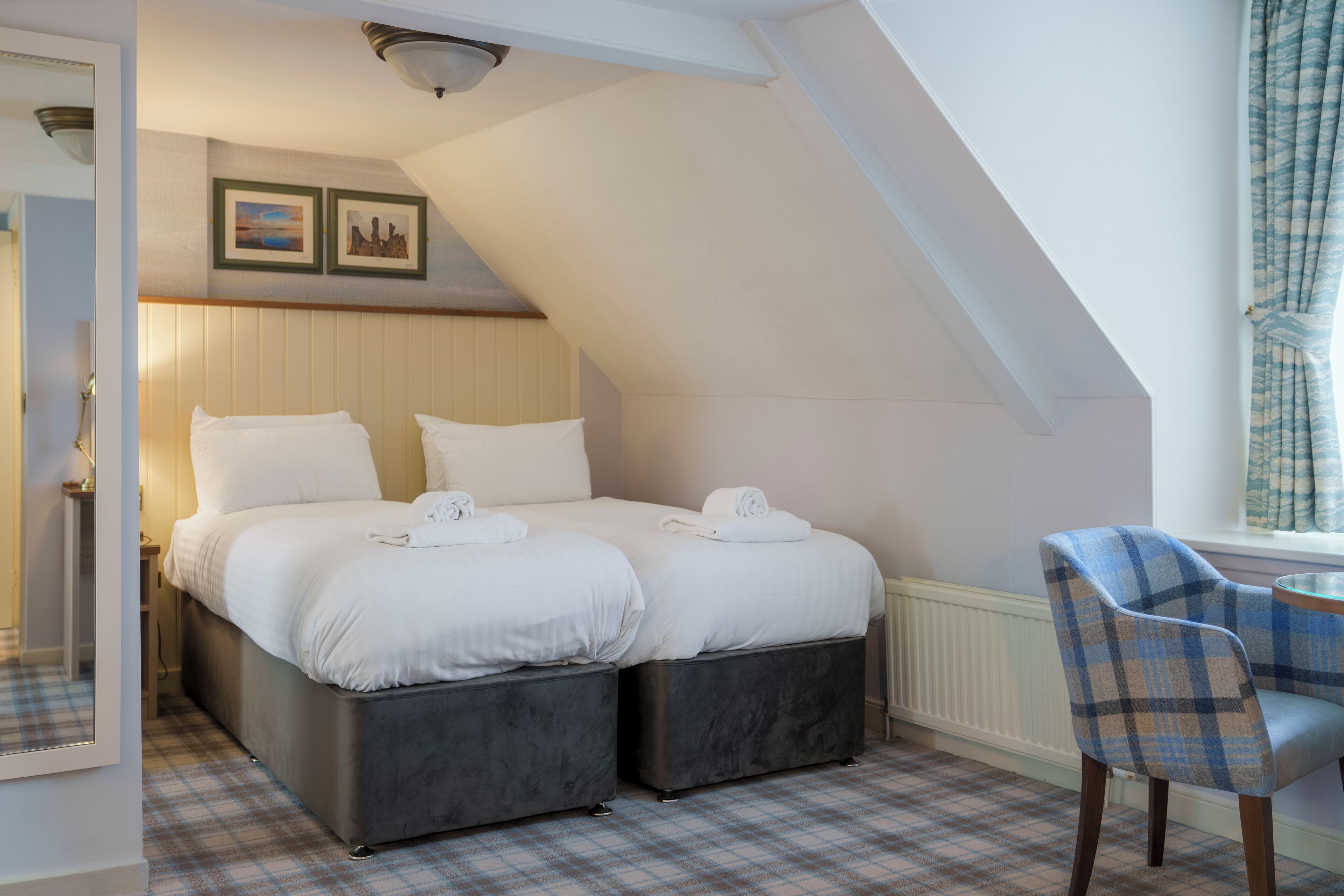A bedroom with a double bed, two bedside tables, a chair, and a window with curtains.