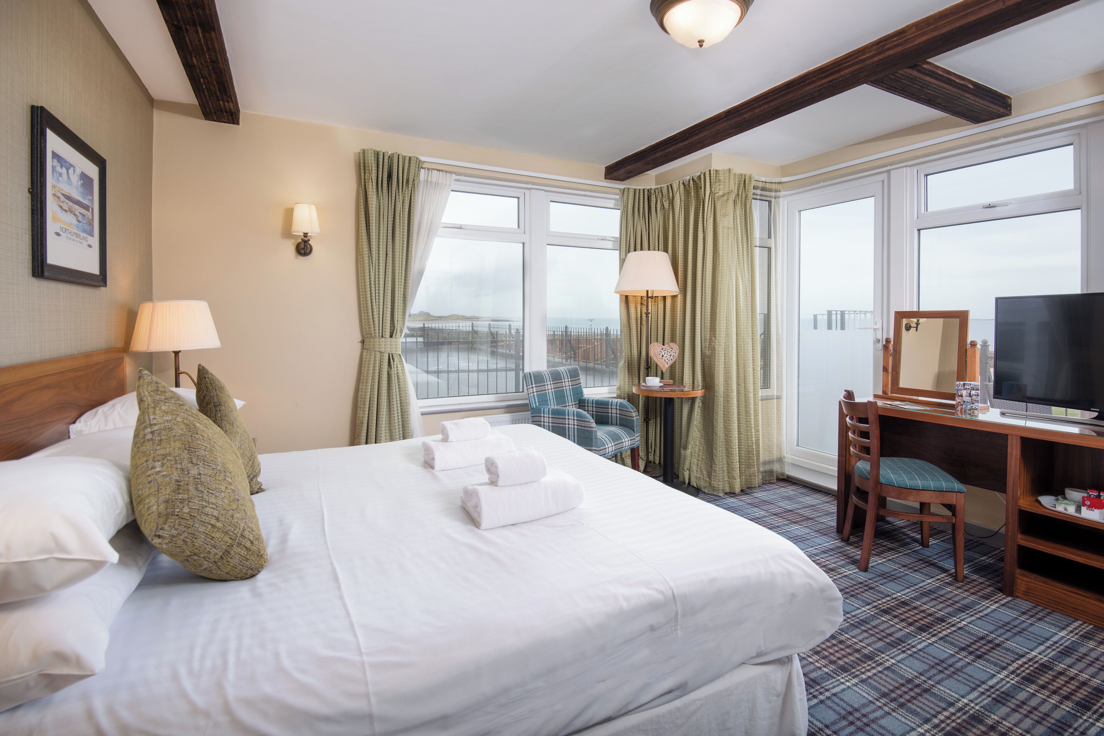 A hotel room with a large bed, a desk with a chair, a television, and a view of the city through the windows.