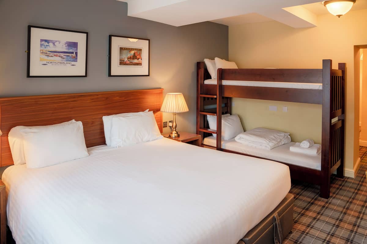 Ein Hotelzimmer mit einem großen Bett, einem Schlafplatz in Form eines Etagenbettes, einem Nachttisch mit Lampe und zwei gerahmten Bildern an der Wand.