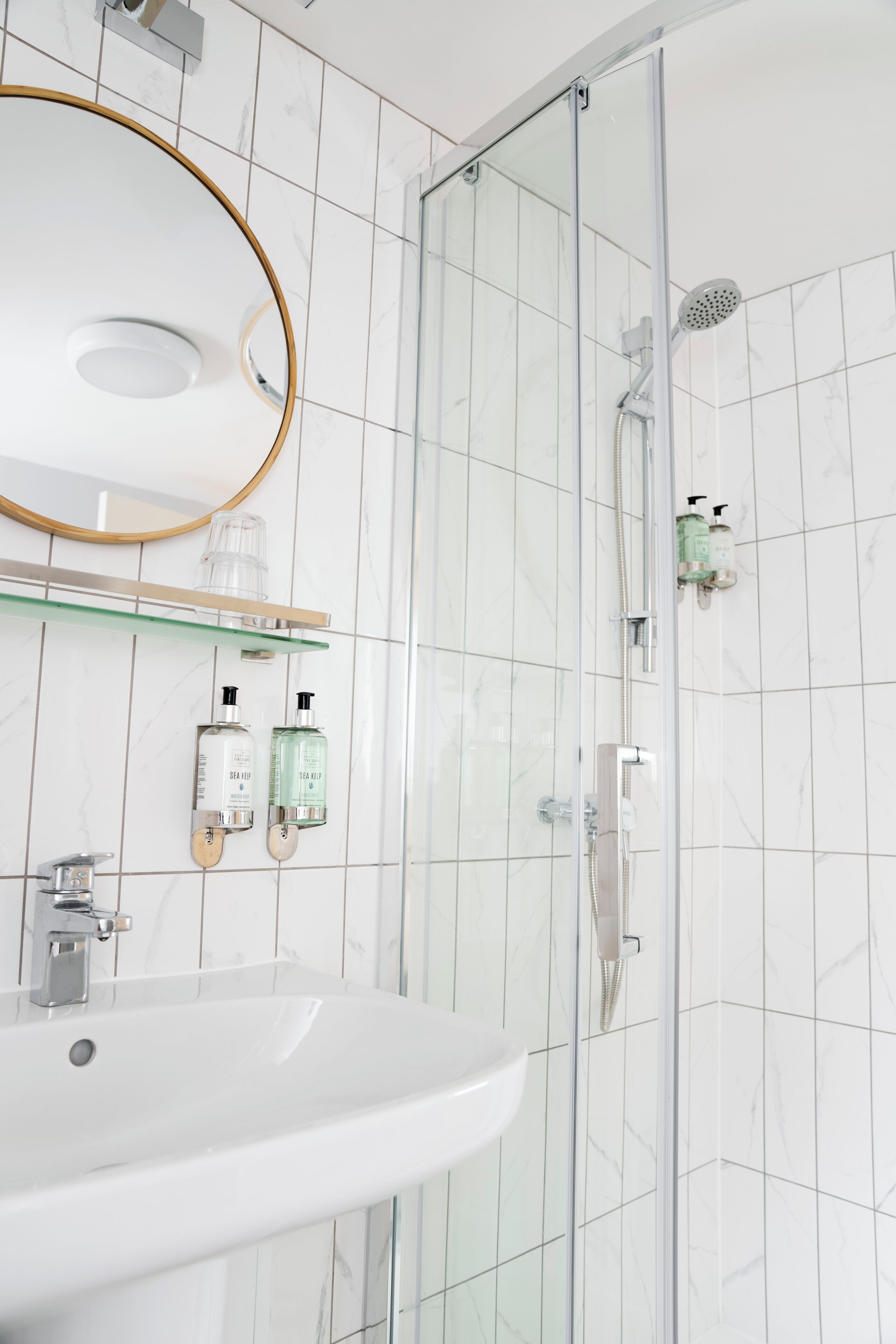 Un bany modern amb dutxa envidriada, un lavabo blanc i un mirall amb marc daurat.