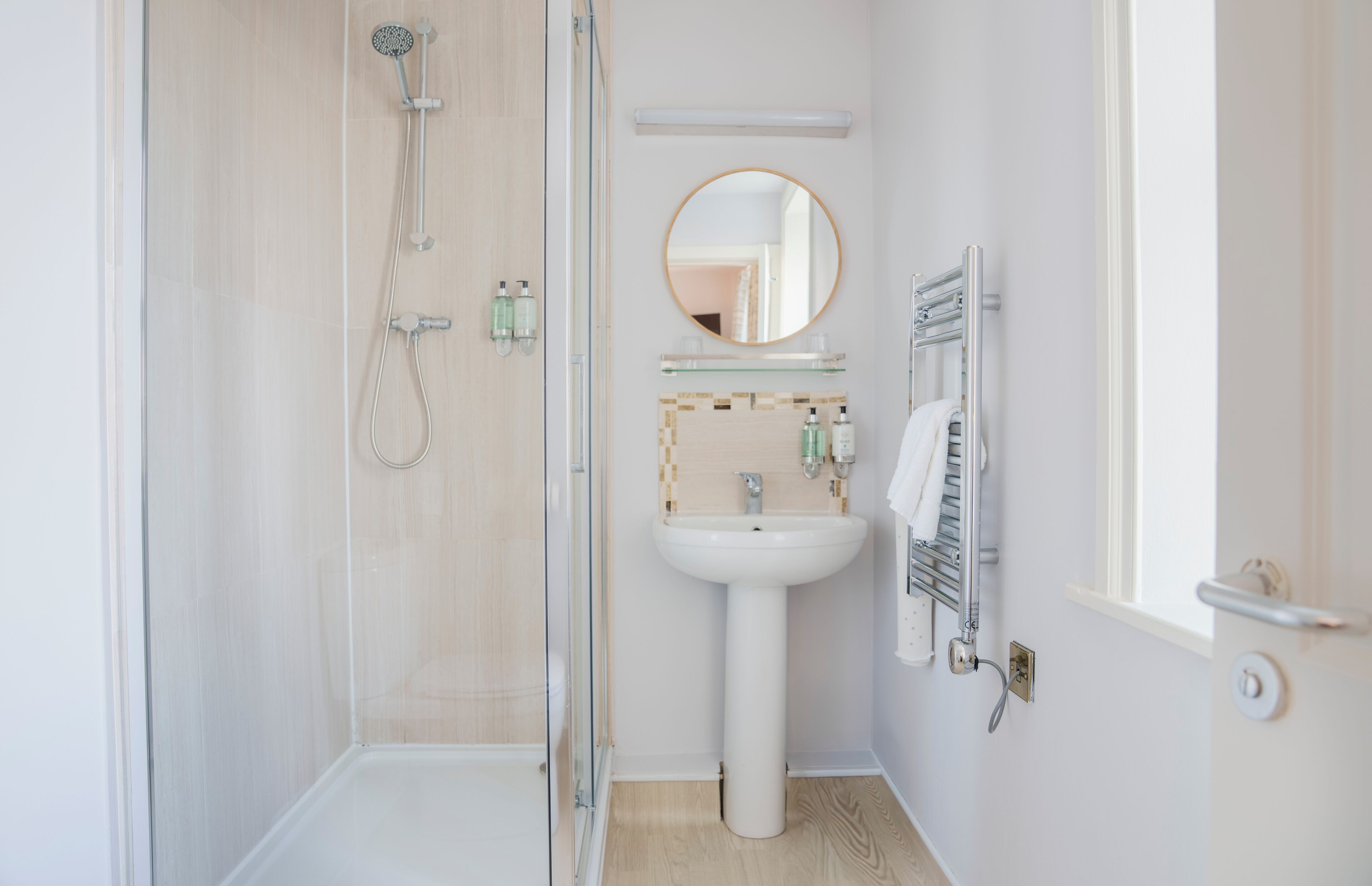 A bathroom with a glass shower enclosure, a pedestal sink, a mirror, and a towel rack.