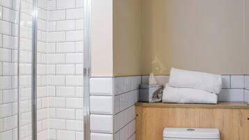A bathroom with a glass-enclosed shower, white tiles, a wooden cabinet, and a white toilet.