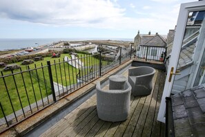A balcony with wicker furniture, a view of the sea, and a parking area with cars.