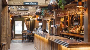 Een bar met een houten toonbank, hangende lampen en een bordje met de richting naar de toiletten.