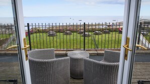 Een balkon met rieten meubels, uitzicht op zee en een omheind tuingedeelte.