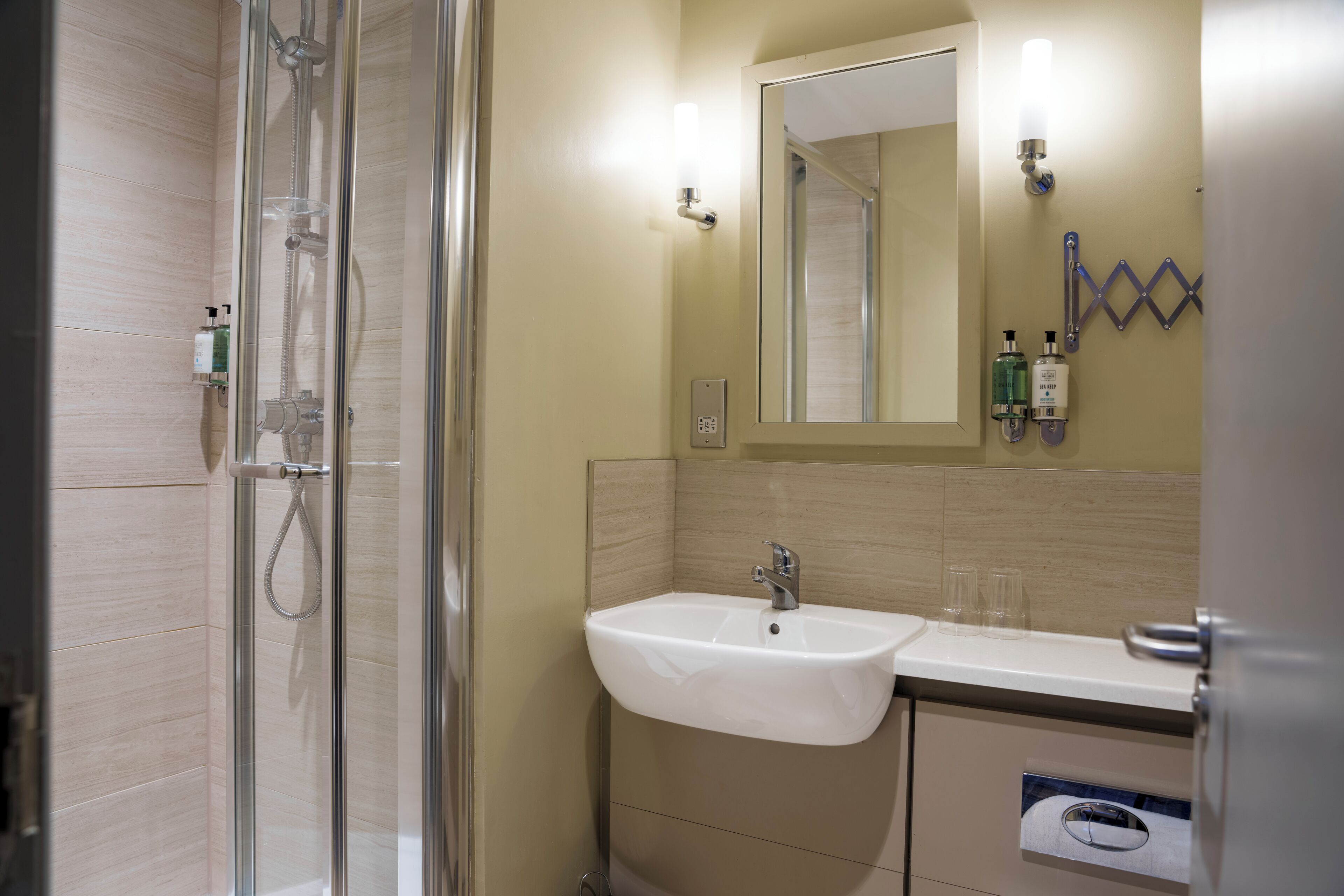 A bathroom with a glass-enclosed shower, a white sink, and a mirror above it.