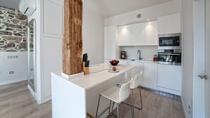 Eine moderne Küche mit weißen Schränken, einer Holz-Akzentstütze, einem eingebauten Herd und einer kleinen Bar mit weißen Stühlen.