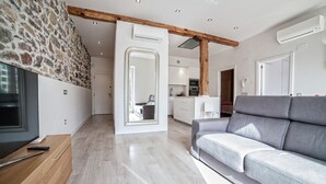 Ein modernes Wohnzimmer mit Steinwand, grauem Sofa und Holzbalken an der Decke.