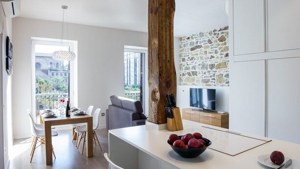 Eine moderne Küche mit Steinwand, einem Essbereich mit Tisch und Stühlen sowie einem großen Fenster mit Blick auf Gebäude.