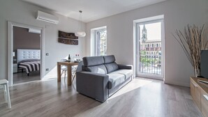 Ein modernes Wohnzimmer mit einem grauen Sofa, einem Esstisch mit Stühlen und einem großen Fenster mit Blick auf ein Gebäude.