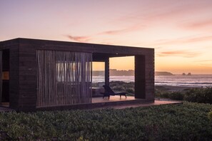 Una estructura moderna de madera con un muro de cristal que da al océano al atardecer.