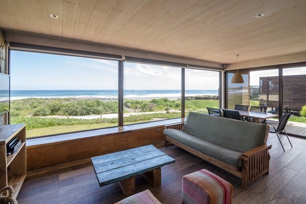 Un amplio espacio al aire libre con una terraza de madera, un sofá, una mesa y vista al océano.