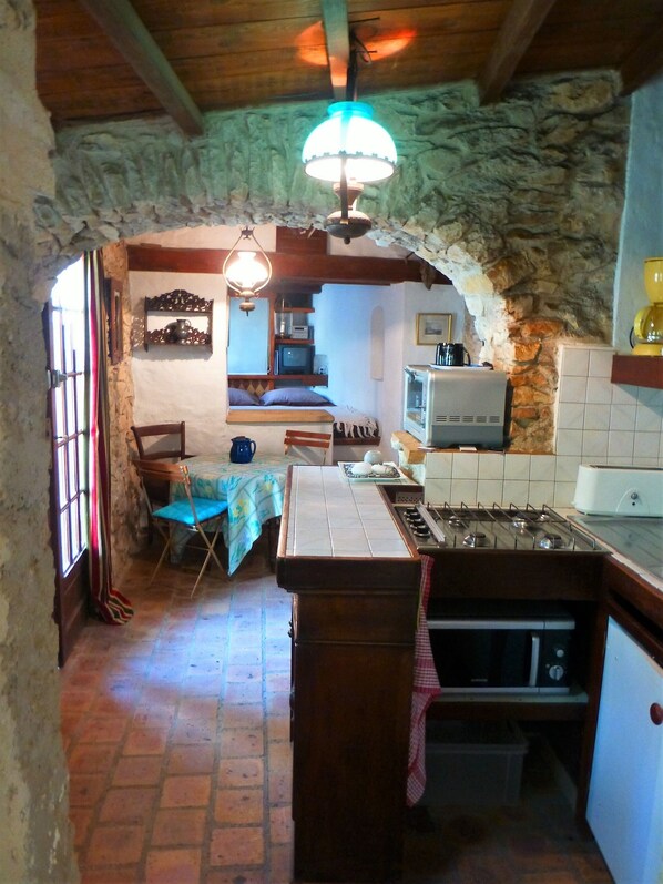 A rustic kitchen with a central island, a dining area with a table and chairs, and a bedroom with a bed and a television. - Rental Mazet stone between Nimes and Montpellier (Souvignargues)