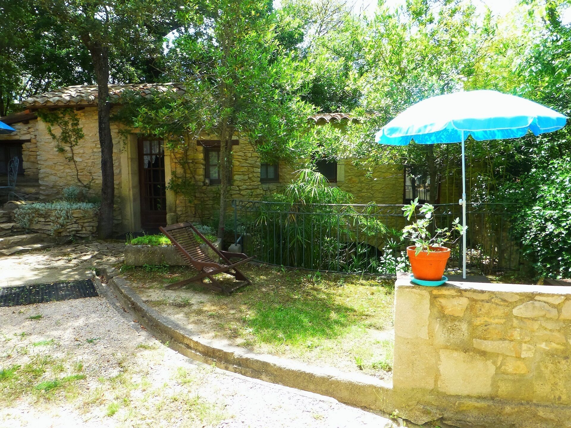 A stone house with a garden, a wooden bench, and a blue umbrella.