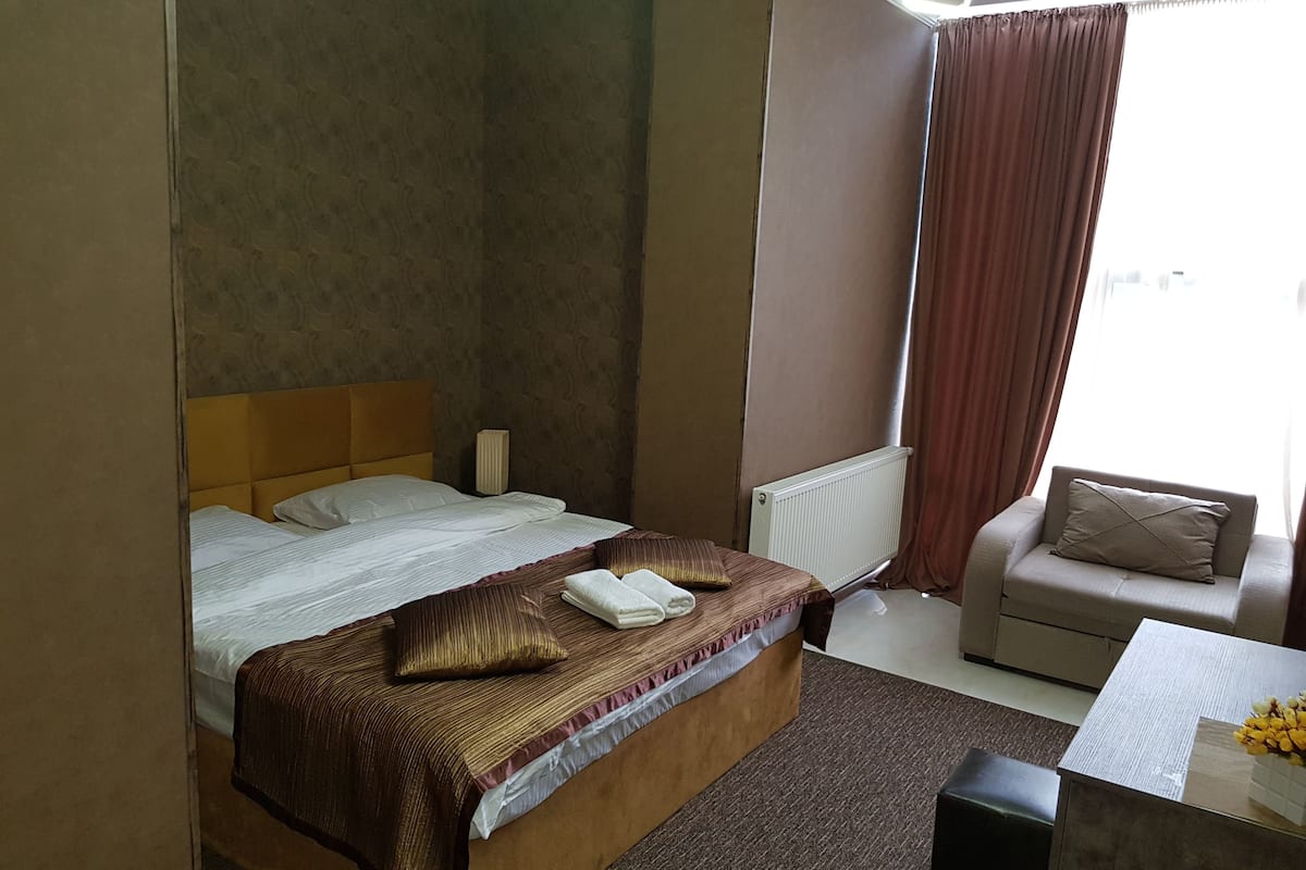 Una habitación de hotel con cama, sofá, radiador y ventana con cortinas.