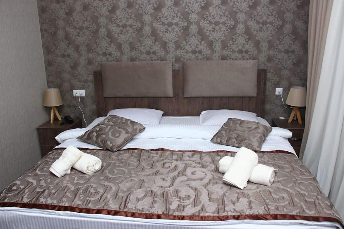 Una cama bien tendida con una colcha estampada, dos almohadas y toallas enrolladas sobre un cabecero de madera.