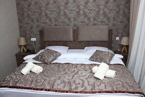 Cama bem arrumada com colcha estampada, dois travesseiros e toalhas dobradas em um painel de cabeceira de madeira.