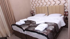A neatly made bed with a floral-patterned bedspread, a headboard with a unique wavy design, and two bedside tables with lamps. - Hotel Makona (Tbilisi)