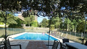 Une piscine rectangulaire, bordée d’une terrasse carrelée et entourée d’une clôture. On y trouve des chaises longues et une table avec des chaises disposées autour de la piscine.
